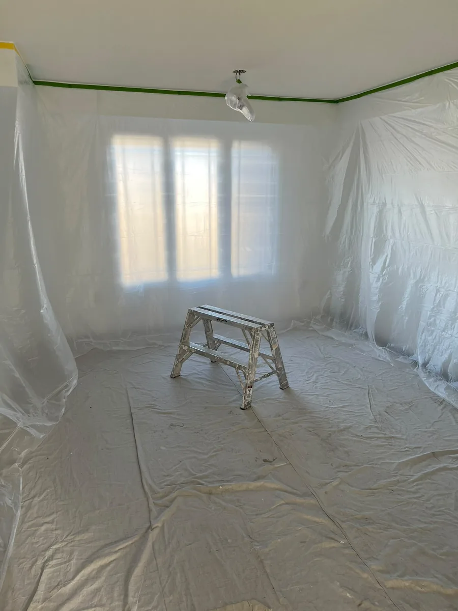 Room prepared for ceiling work with walls and windows covered in sheeting and floors protected